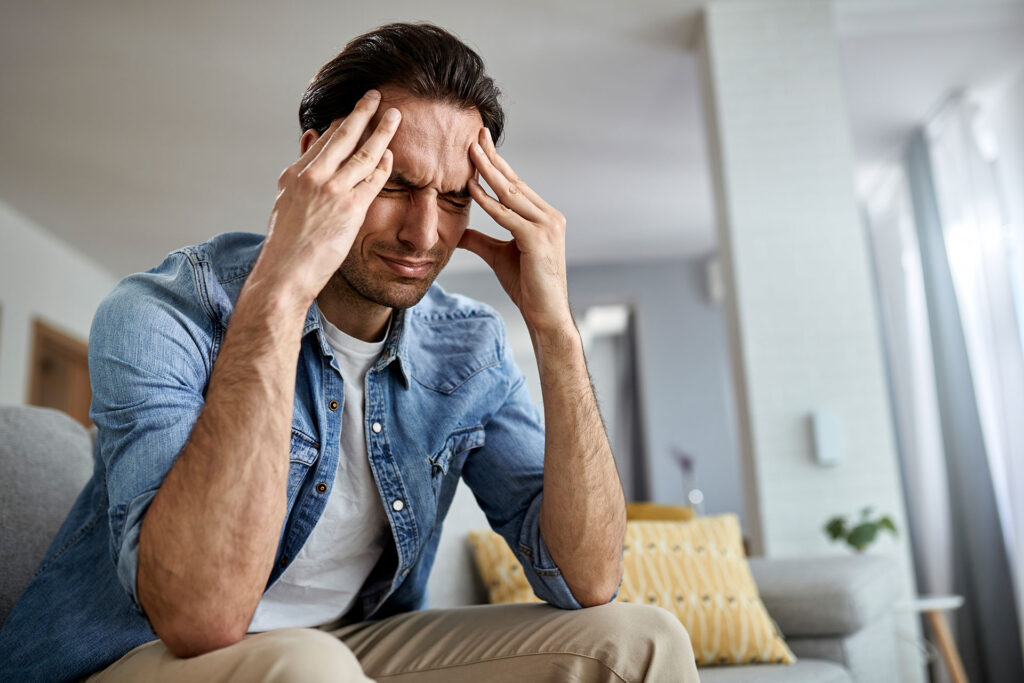 Man experiencing stress and holding his head while sitting on a couch - LeaveConsult