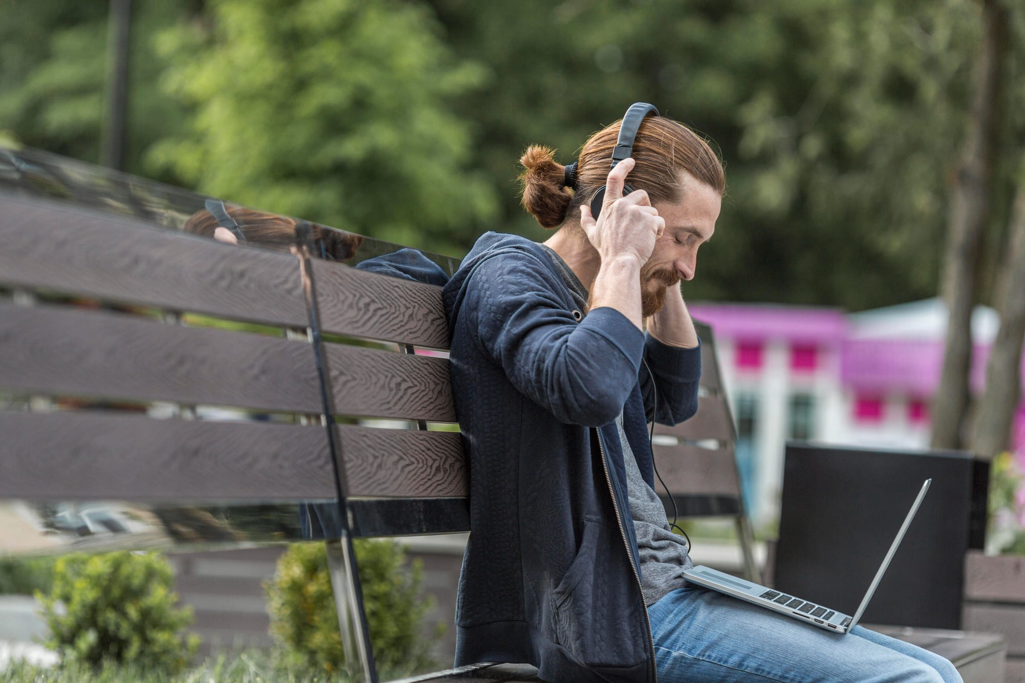 Man sitting on a park bench using headphones and a laptop outdoors - LeaveConsult